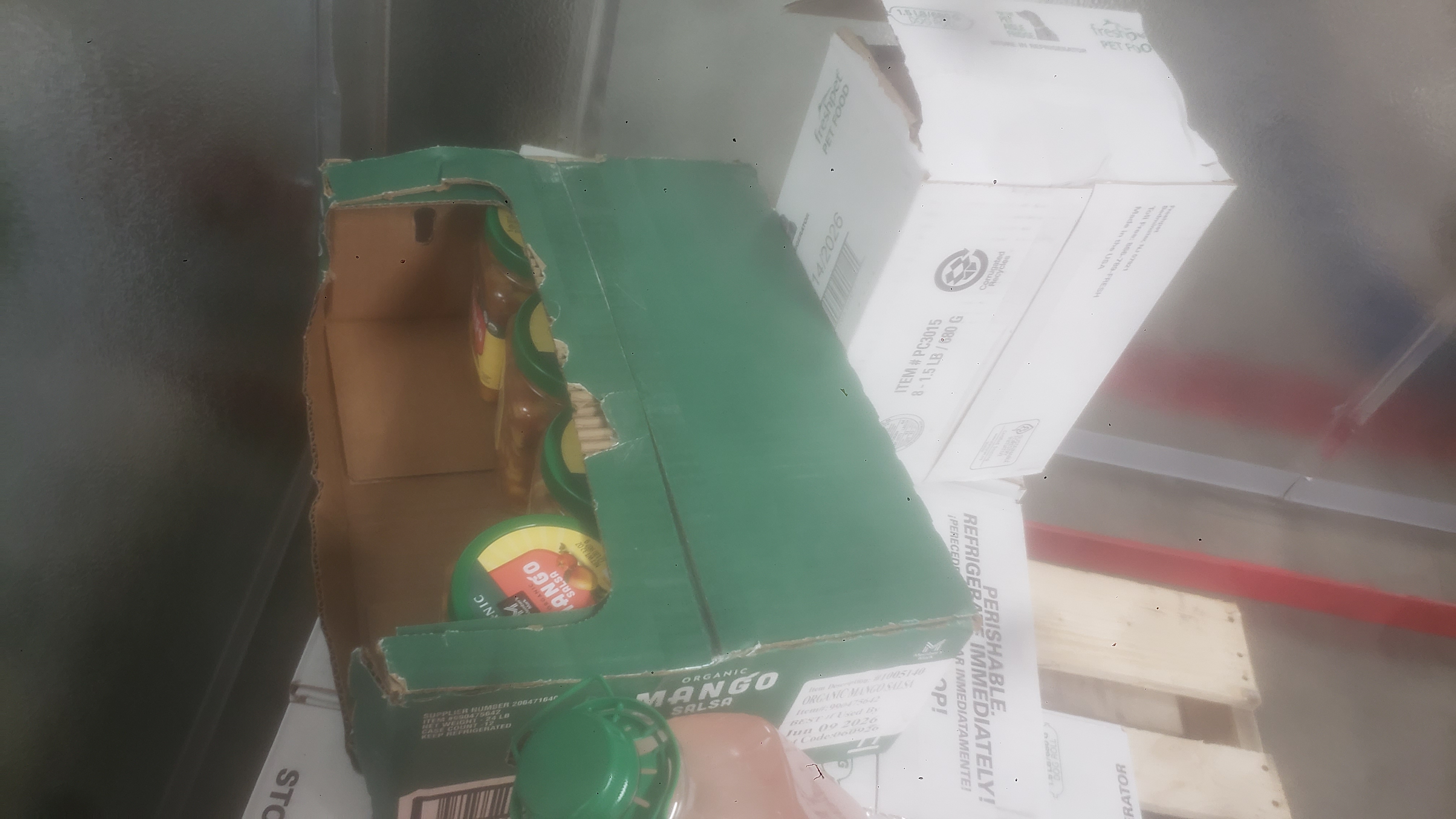 Jars of mango salsa in a shipping tray on top of boxes of pet food.